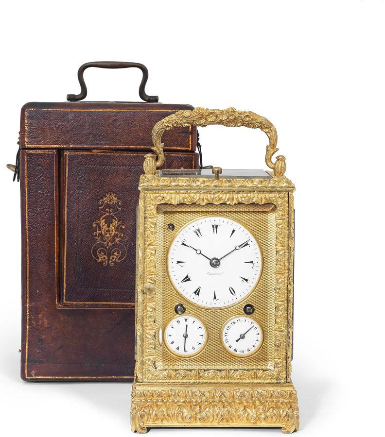 Gilt-bronze carriage clock with white enamel dials beside its leather travel case