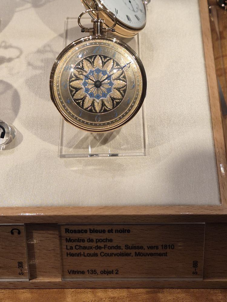 Museum vitrine with a gold pocket watch with a blue and black rosette dial and its label