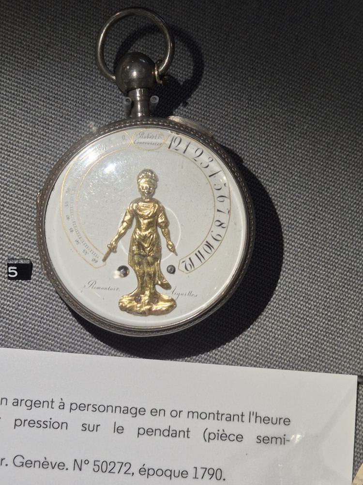 Silver pocket watch with a gold figure indicating the hour, in a museum vitrine
